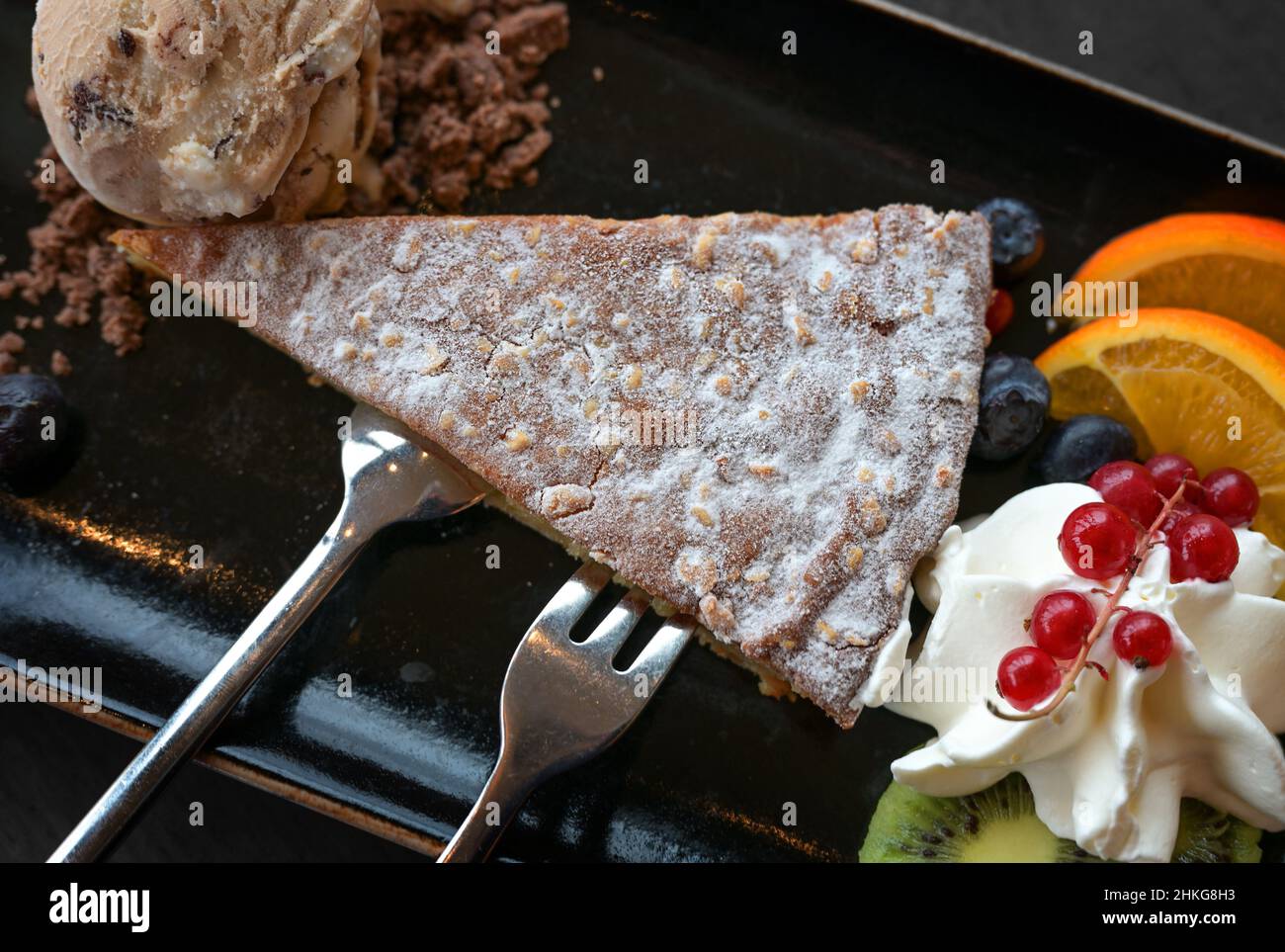 Dessert da torta di mandorle fatta in casa con gelato e frutta fresca su un piatto nero con posate, vista dall'alto Foto Stock