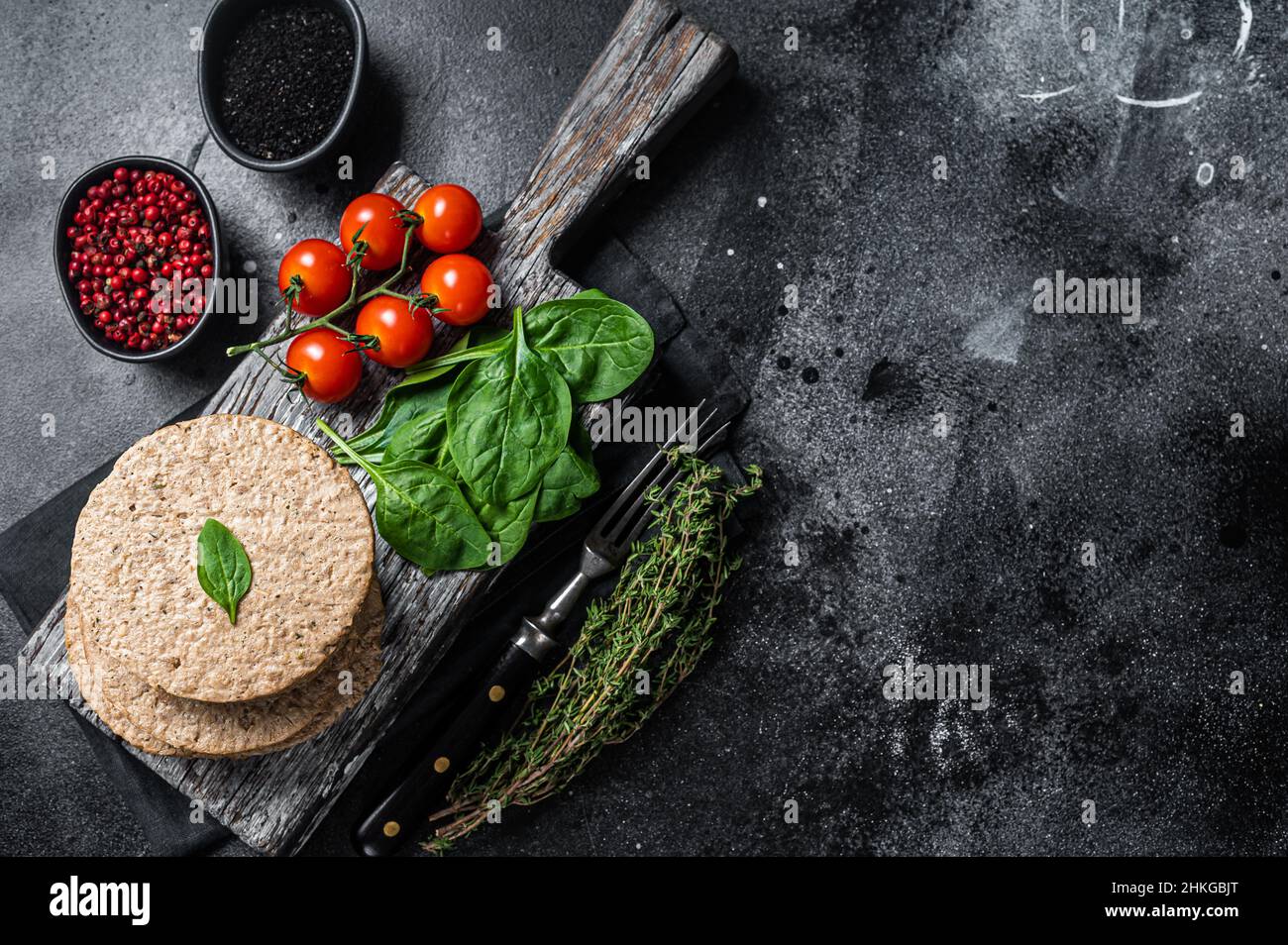 Polpettine vegetariano a base di carne di hamburger, cotolette vegane crude su tavola di legno con erbe. Sfondo nero. Vista dall'alto. Spazio di copia Foto Stock