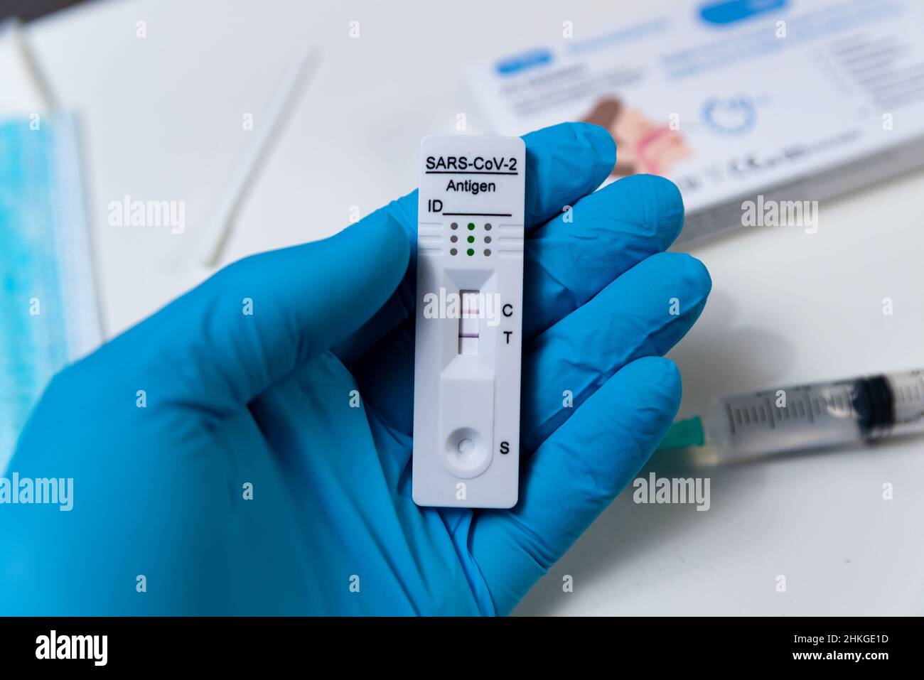 Una mano che indossa un guanto protettivo è vista che tiene un test rapido di Covid, anche noto come test dell'antigene o test di flusso laterale, che mostra un risultato positivo in un Foto Stock