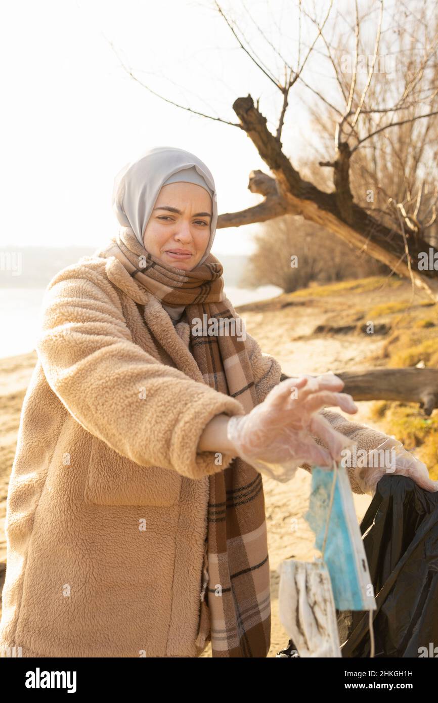 Volontariato pulizia e mostrando disgusto quando si raccoglie una maschera usata Foto Stock