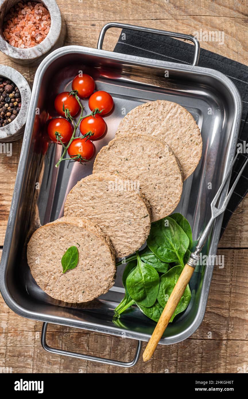 Polpette crude senza carne a base di carne vegetale, crocchette di hamburger vegano fresco in vassoio da cucina con erbe. Sfondo in legno. Vista dall'alto Foto Stock