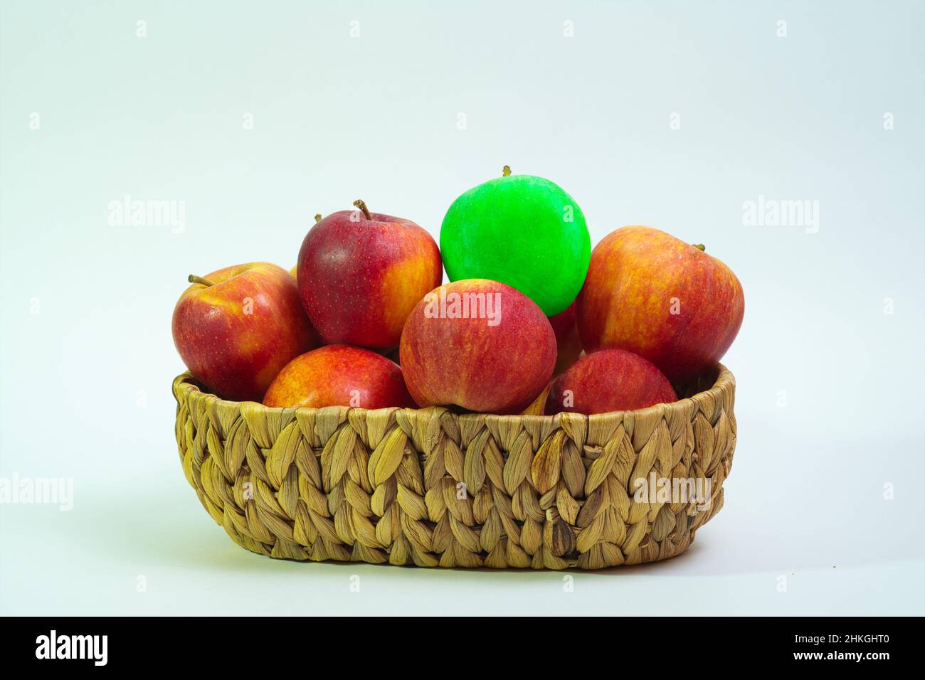 una mela verde tra molte mele rosse in un cestino Foto Stock