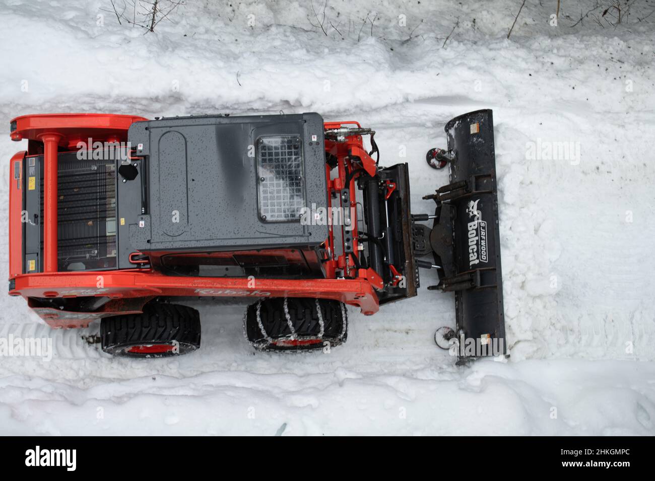 Piccolo spazzaneve che muove la neve sul sentiero come visto dall'alto con catene sugli pneumatici invernali dopo una tempesta di neve nel piccolo villaggio sciistico della Columbia Britannica Foto Stock