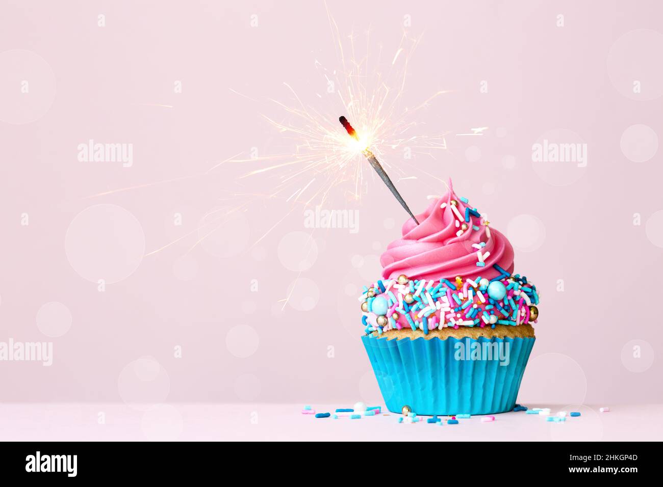 Cupcake di compleanno con festeggiamenti scintillanti e colorati spolverini di zucchero rosa e blu Foto Stock