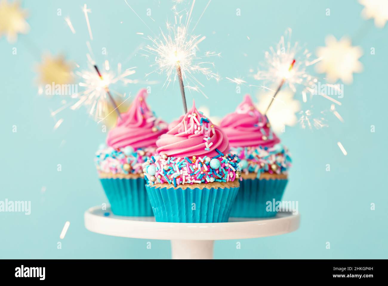 Tre cupcake di compleanno con glassatura rosa e festeggiatori scintillanti Foto Stock