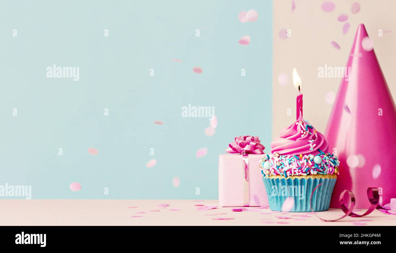 Sfondo di compleanno con cupcake e candela di compleanno rosa, regalo di compleanno e cappello da festa Foto Stock