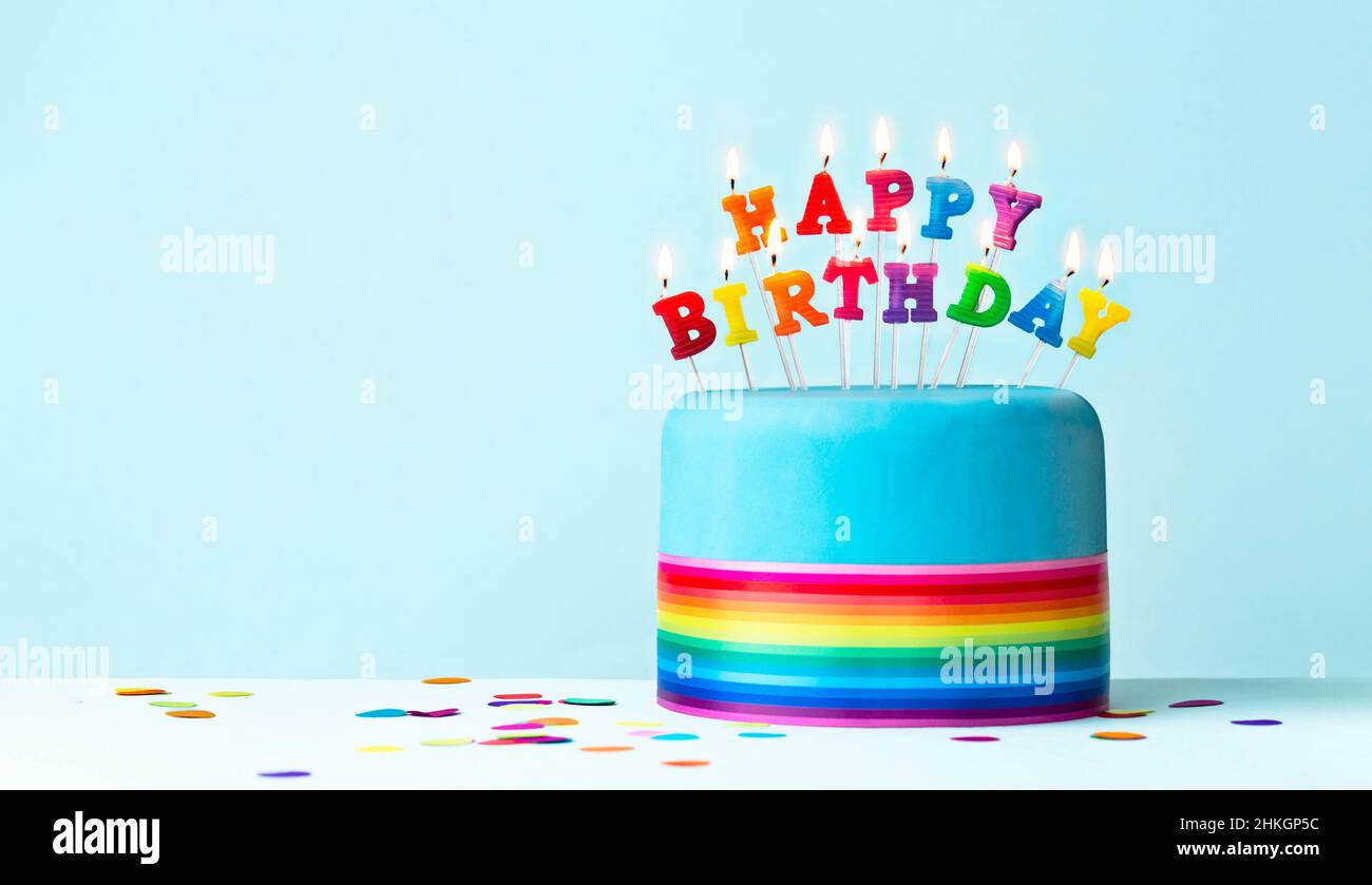 Torta di compleanno arcobaleno colorata con nastro arcobaleno e candele di compleanno arcobaleno Foto Stock