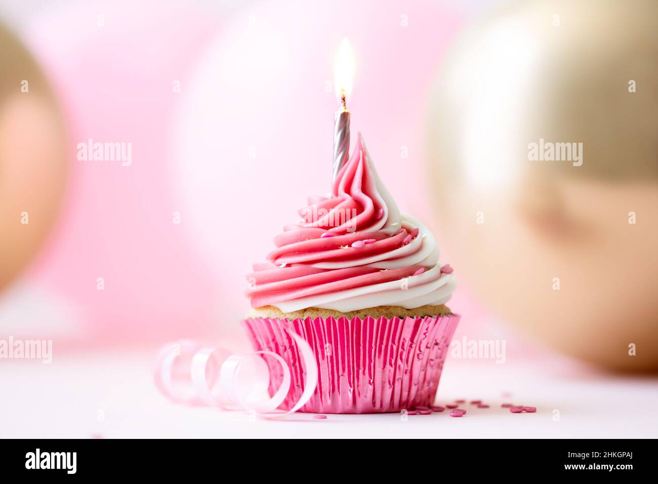 Cupcake rosa di compleanno con una candela dorata su sfondo di palloncini rosa e oro Foto Stock