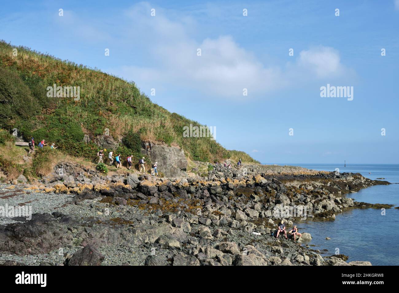 Un gruppo di escursionisti segue lo stretto sentiero che segue la costa rocciosa intorno alla penisola di Porth Dinllaen, Galles Foto Stock