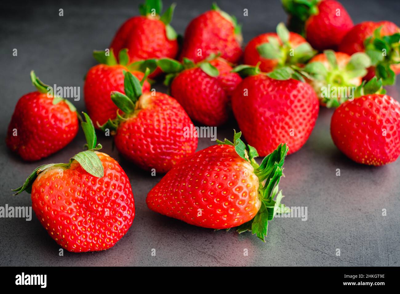 Fragole intere fresche su sfondo scuro: Raggruppamento di bacche rosse mature su un piano in pietra scura Foto Stock