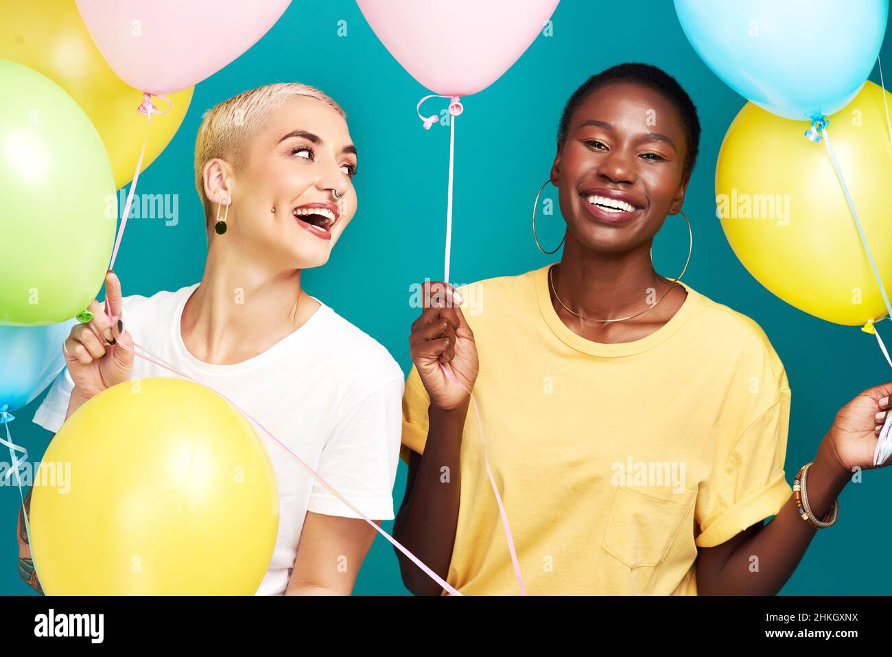 Buon giorno di amicizia. Studio girato di due giovani donne tenendo un mazzo di palloncini colorati su uno sfondo turchese. Foto Stock