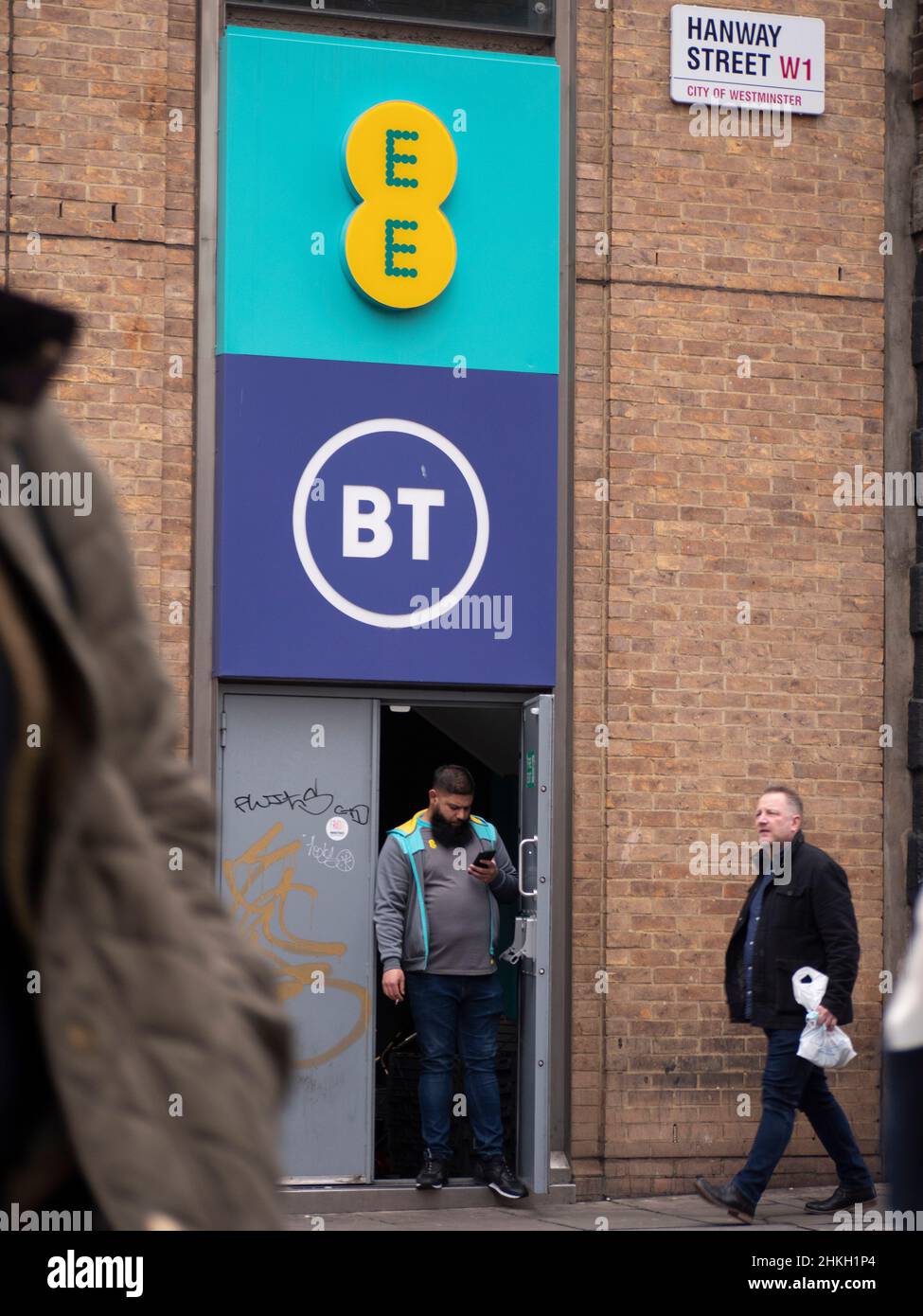 Tutto ovunque EE e British Telecom BT, edificio nel centro di Londra con il lavoratore che prende una pausa sigaretta in porta, guardando il telefono cellulare Foto Stock