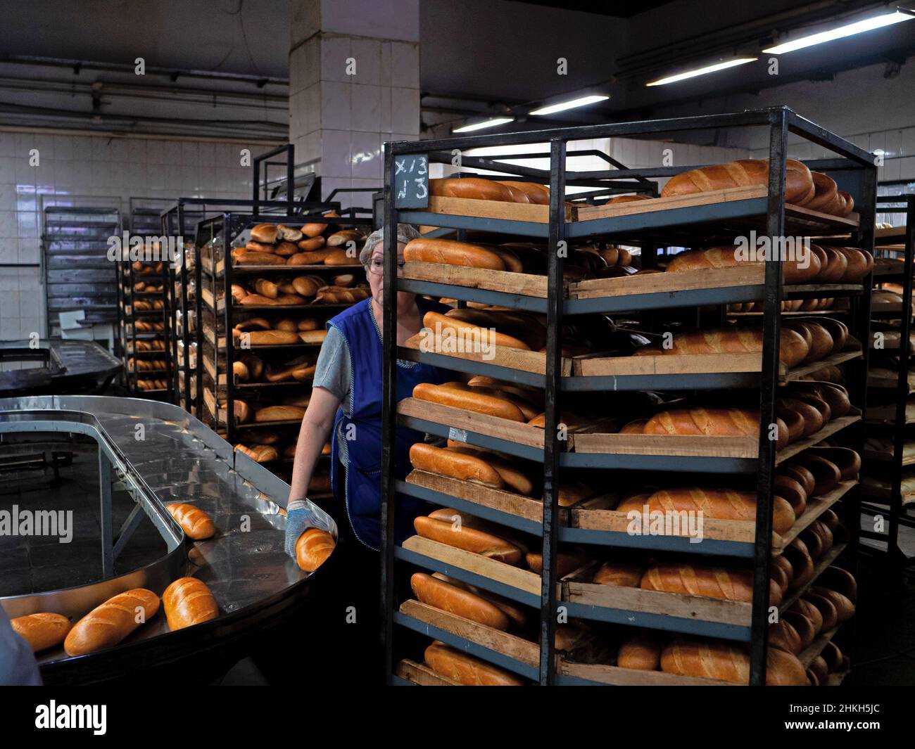 Kazan, Russia. Febbraio 02, 2022. Un addetto alla panetteria sul nastro trasportatore. Rack di pane fresco. Pane appena sfornato. Pane fresco su una rastrelliera mobile con s Foto Stock