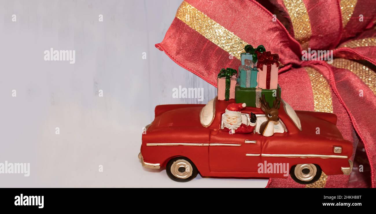 Banner natalizio con giocattolo babbo natale in un'auto retrò con una renna e un mucchio di regali in cima su uno sfondo chiaro con un nastro di Natale - stanza Foto Stock