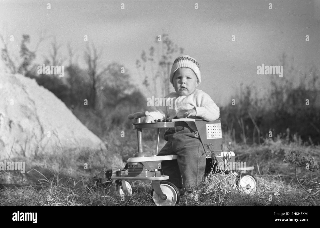 1940s, storico, esterno, un bambino seduto in un passeggino Taylor Tot, USA. Noto anche come baby walker, aveva una base in legno e un telaio laterale in metallo dove il bambino sarebbe seduto e un piccolo 'diving' maniglia in legno sulla parte anteriore per sterzare. Quattro ruote in metallo e un poggiapiedi. Realizzato dalla Frank F. Taylor Company, questo è stato il primo passeggino del 20th secolo. Taylor ha iniziato la sua attività a Cincinnati, Ohio, nel 1921 al 2801 di Highland Avenue. Vi rimase fino al 1964, quando fu ricollocato a Frankfort, KY. Foto Stock