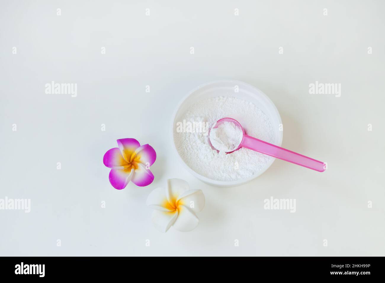 polvere bianca cosmetica con cucchiaio in contenitore di plastica vicino al fiore di frangipani o proteine grani fini Foto Stock