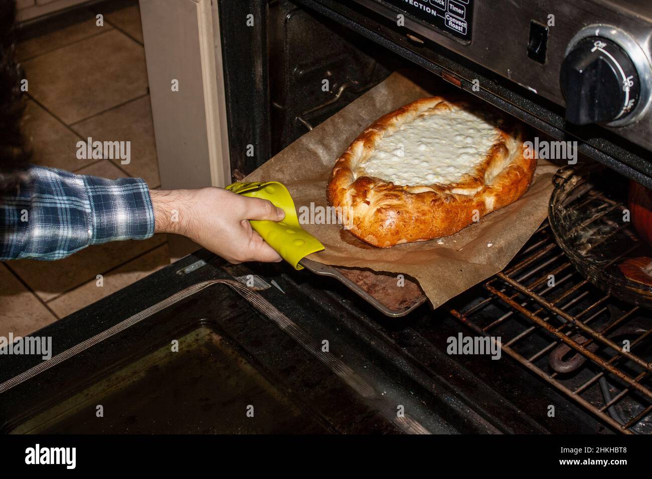 Togliere a mano il khachapuri georgiano dal forno con pane rosolato e formaggio gorgogliante Foto Stock