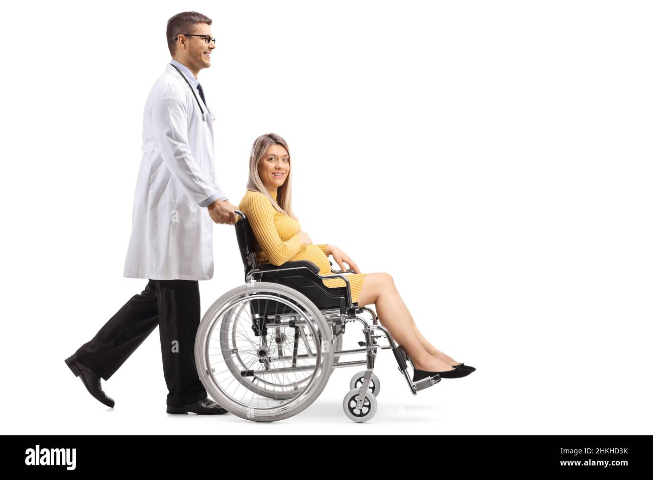 Colpo di profilo a tutta lunghezza di un medico di sesso maschile che spinge una donna incinta in una sedia a rotelle isolata su sfondo bianco Foto Stock