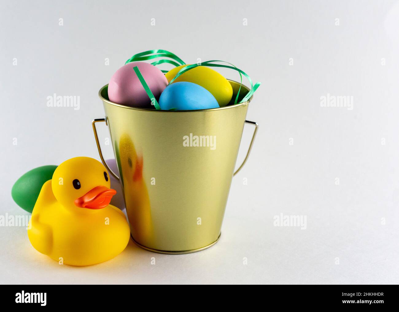 Anatra di gomma e un secchio di uova pasquali pastello su sfondo bianco con spazio copia. Foto Stock