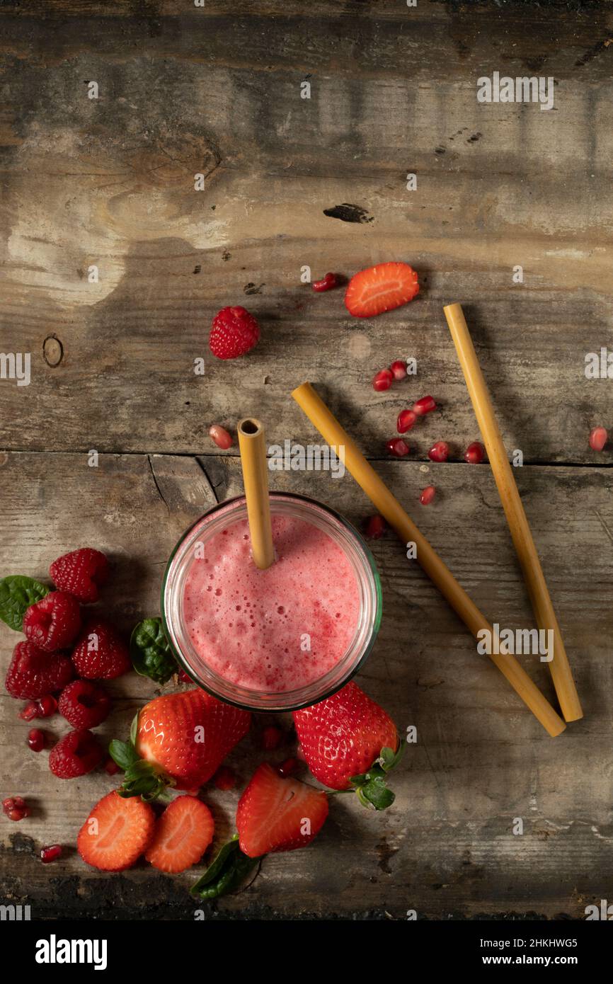 bevanda frullato di bacche rosse con cannucce di bambù circondate da ingredienti verdi su una superficie rustica di legno adagiato piatto da sopra lo spazio di copia Foto Stock