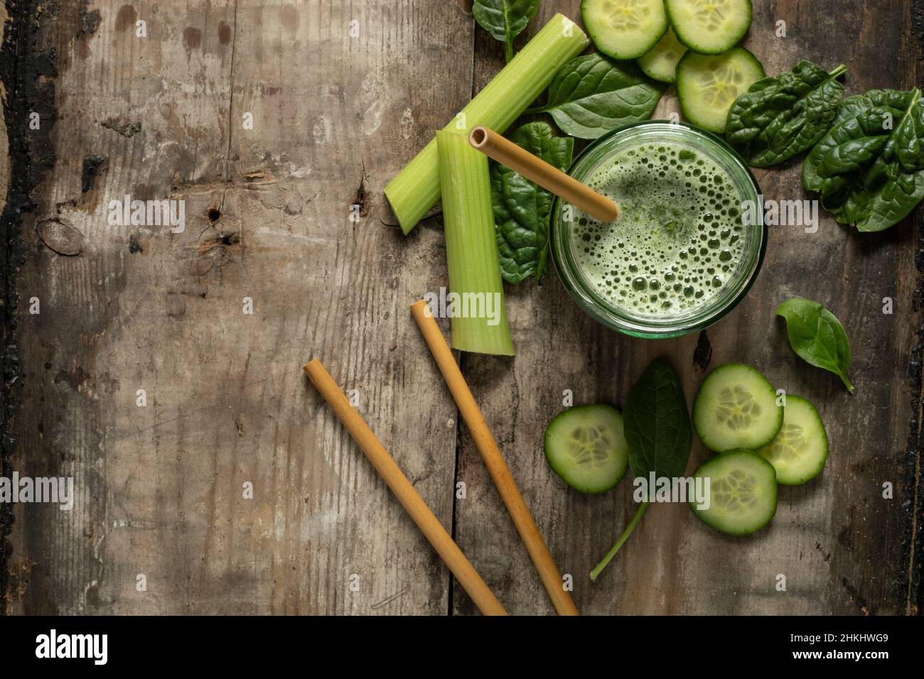 Bevanda frullato verde con cannucce di bambù circondate da ingredienti verdi su una superficie rustica di legno adagiato piatto da sopra lo spazio di copia Foto Stock