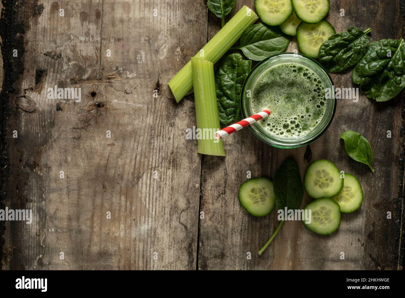 Bevanda frullato verde con paglia di carta rossa e bianca circondata da ingredienti verdi su una superficie rustica di legno adagiato piatto da sopra spazio copia su lef Foto Stock