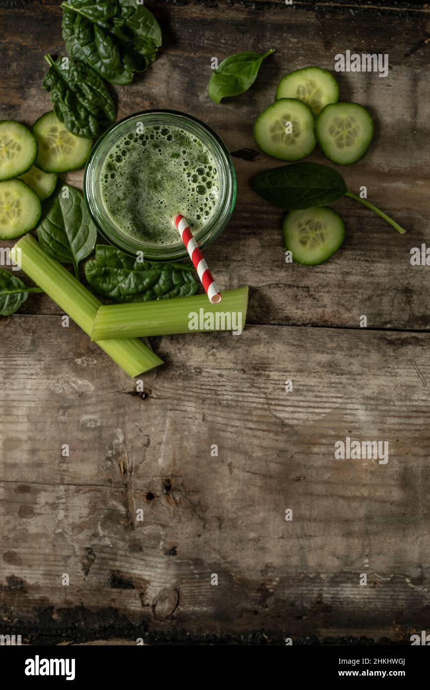 Bevanda frullato verde con paglia di carta rossa e bianca circondata da ingredienti verdi su una superficie rustica di legno adagiata in piano da sopra lo spazio di copia Foto Stock