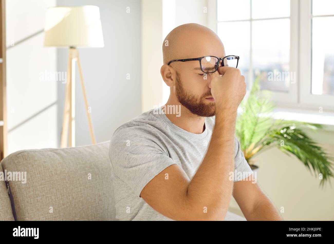 L'uomo che soffre di tensione oculare toglie i suoi occhiali e gli sfrega gli occhi stanchi Foto Stock