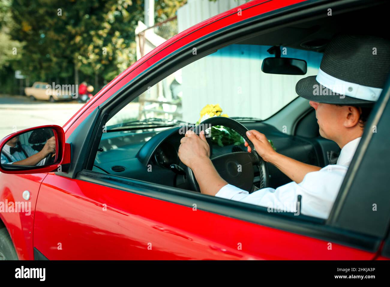 Giovane uomo in un cappello che guida un'auto. Sul cruscotto dell'auto si  trova un bouquet di fiori bianchi-gialli Foto stock - Alamy