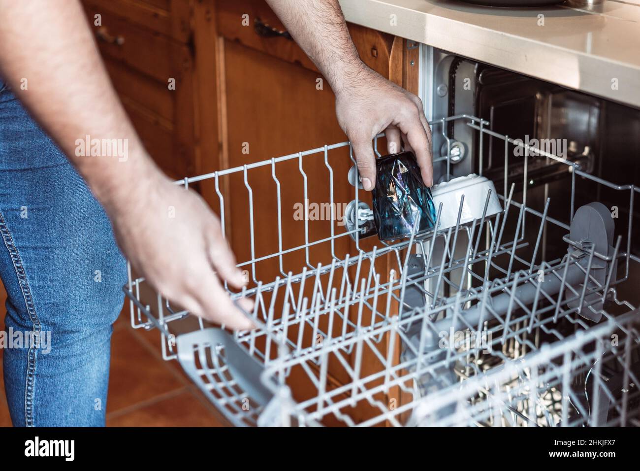 colpo medio delle mani dell'uomo che mette un vetro sporco nella lavastoviglie Foto Stock