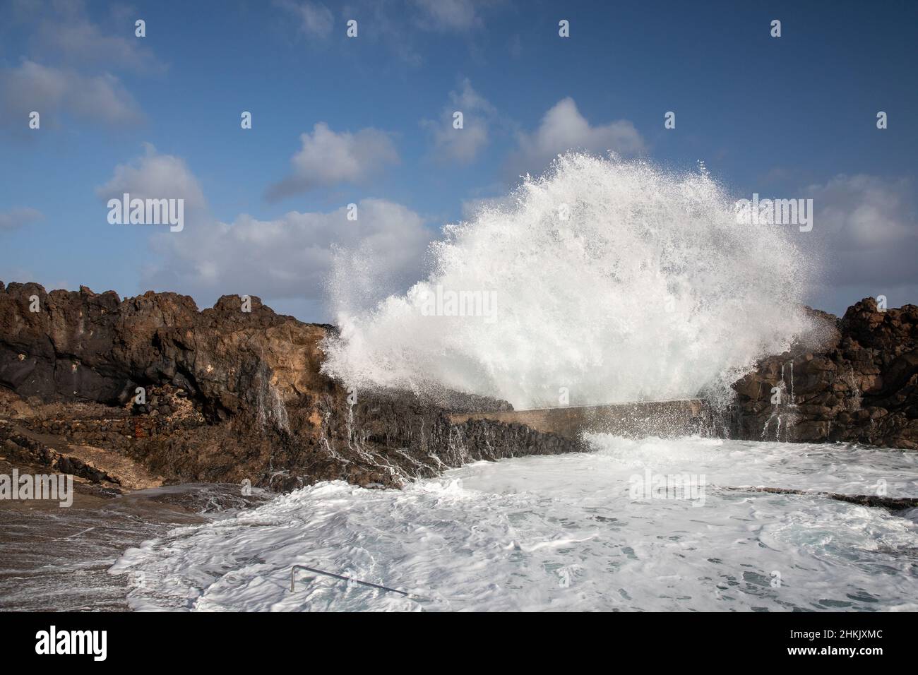 Onde che si infrangono sulla costa rocciosa di fronte alla piscina naturale, Isole Canarie, Lanzarote, Charco del Palo Foto Stock