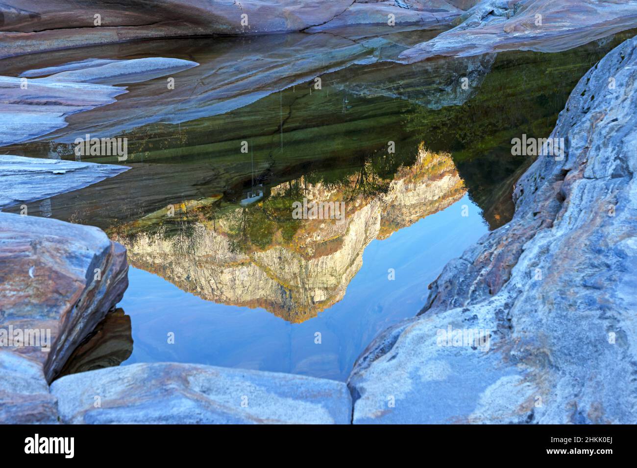 montagna alle spalle di Lavertezzo riflessa in superficie d'acqua tra rocce sul fiume in Val Verzasca, Svizzera, Ticino Foto Stock