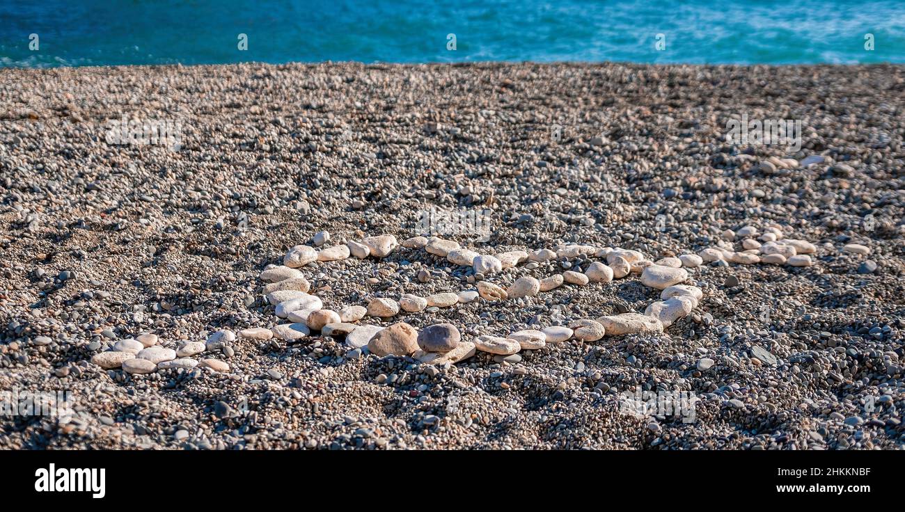 Amore cuore forma su sabbia fatta di ciottoli bianchi, simbolo di amore sulla spiaggia con sfondo mare. San Valentino amore simbolo di forma del cuore, amore Foto Stock