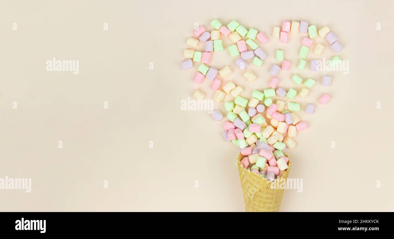 Disposizione con cornet a cono di cialda e marshmallows colorate in forma di cuore su sfondo pastello Foto Stock