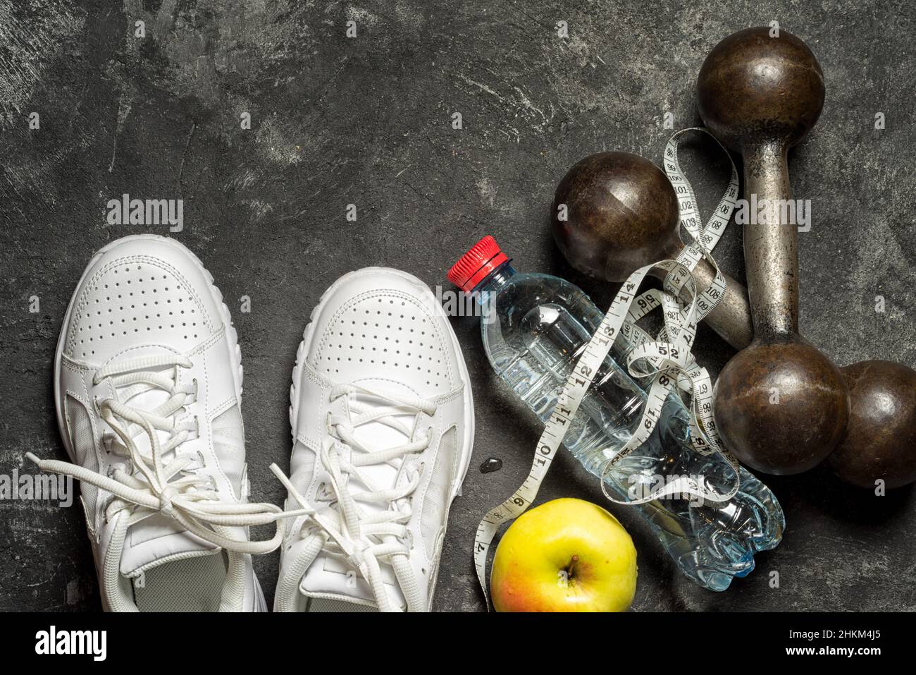 sfondo sportivo vista dall'alto di sneakers, manubri, bottiglia d'acqua, mela e nastro senimetrico su sfondo nero con spazio copia. stile di vita sano Foto Stock