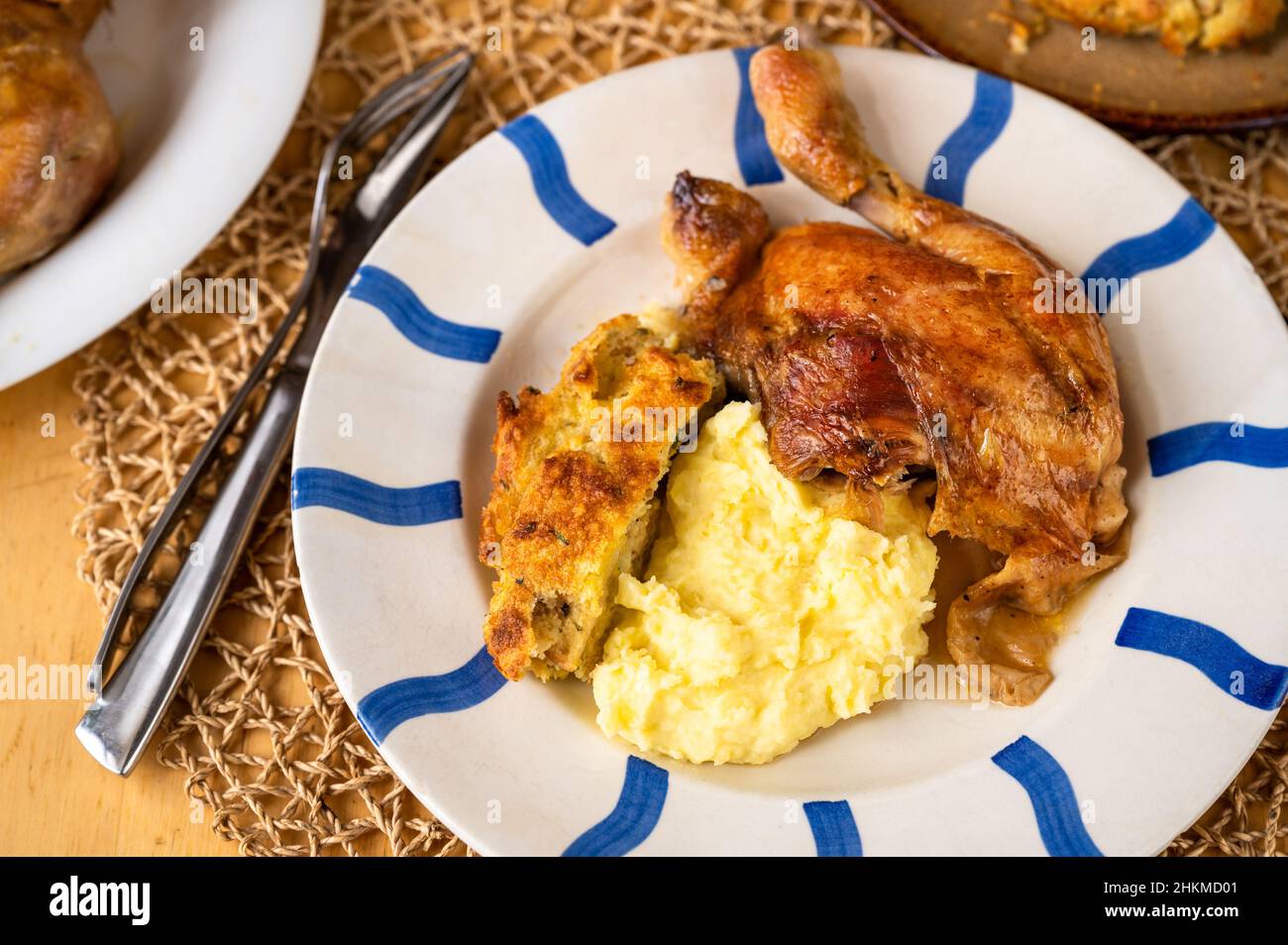 Coscia di pollo al forno, ripieno e purè di patate su piatto a righe sul tavolo. Foto Stock