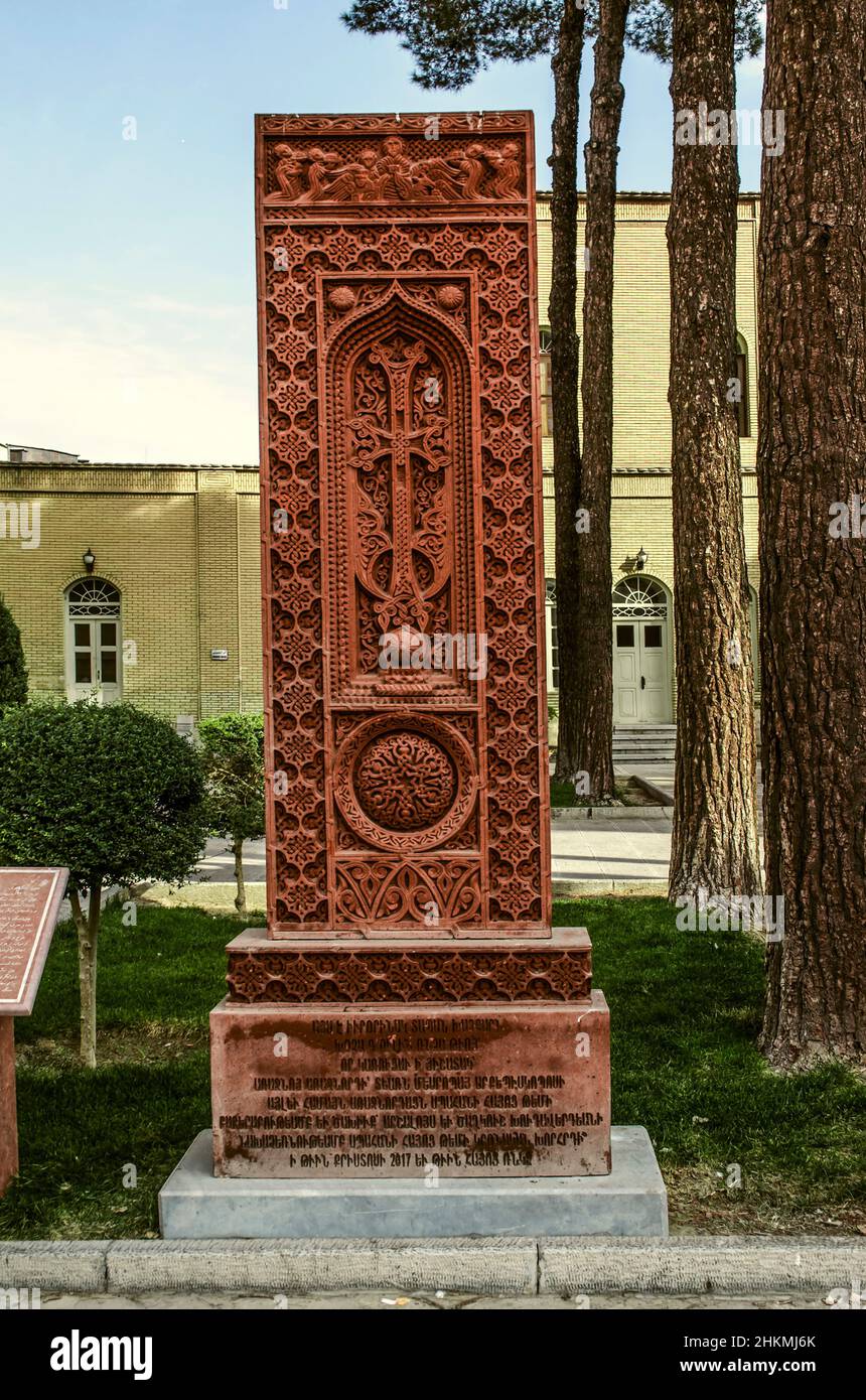 Isfahan, Nor Julfa, Iran, 16 novembre 2021: Khachkar fatto di tufo rosso con una croce di apertura in una cornice di vimini con un simbolo rotondo di eternità, volti Foto Stock