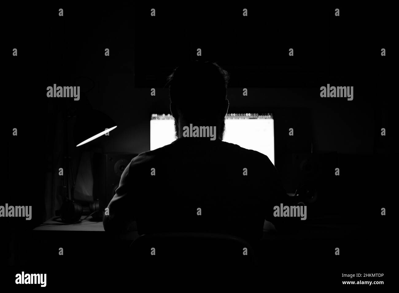 Un uomo si siede ad un computer in una stanza ad un tavolo a nigh programmazione in bianco e nero Foto Stock