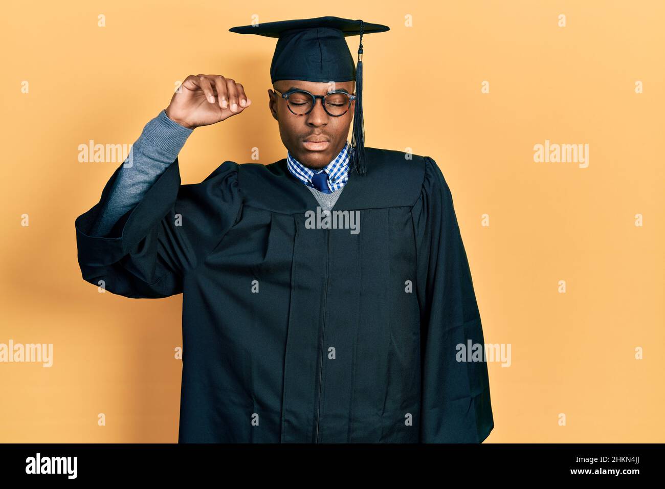 Giovane uomo afroamericano che indossa il cappuccio di graduazione e l'abito da cerimonia che si allunga indietro, stanco e rilassato, assonnato e sbadiglio per la mattina presto Foto Stock