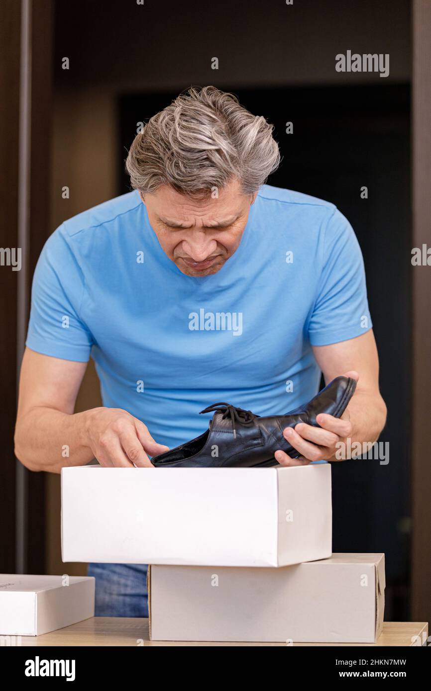 Un uomo è insoddisfatto con l'acquisto di scarpe dal negozio. Prodotto difettoso. Foto Stock
