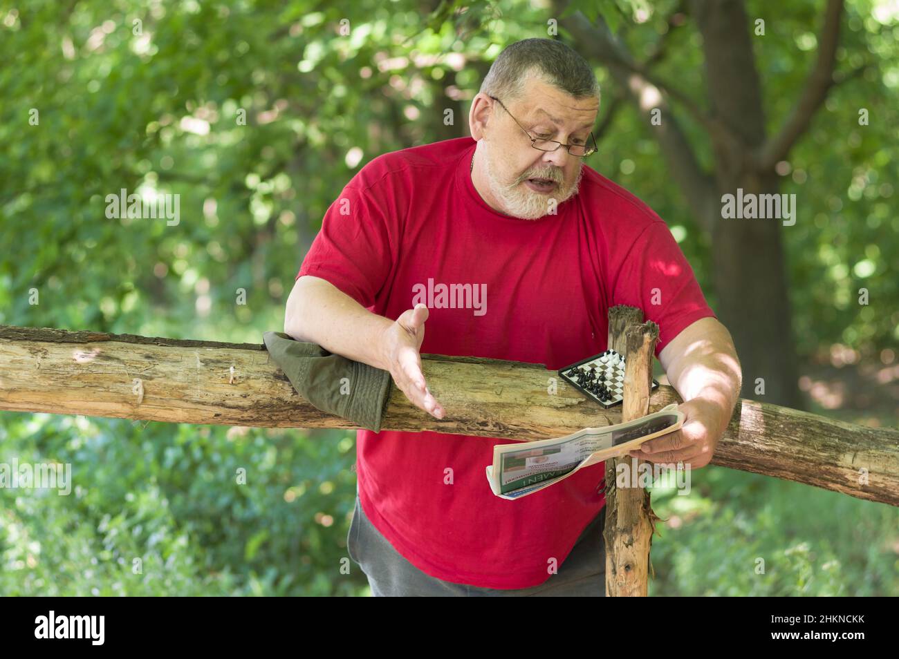 Ritratto di caucasico ported uomo anziano lettura giornale nel parco estivo e non piace l'articolo Foto Stock