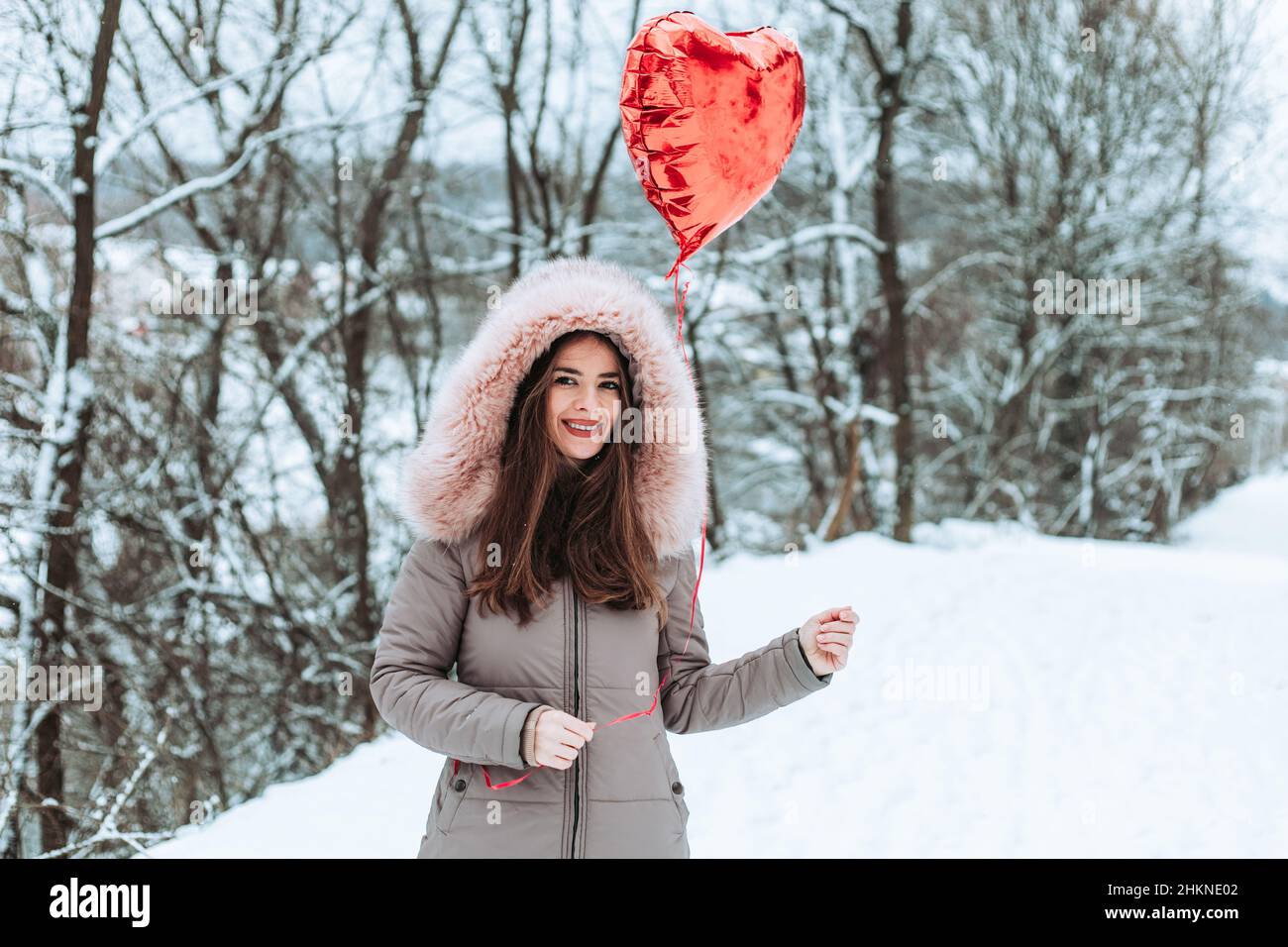 Ragazza in pelliccia giacca che tiene rosso elio cuore a forma di palloncino. San Valentino Foto Stock