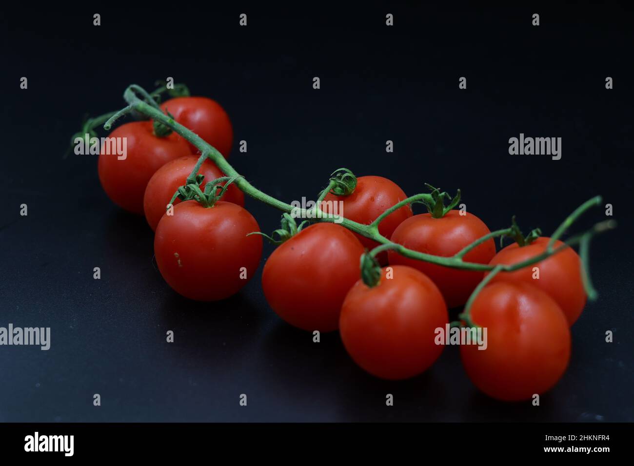 Ramoscello con pomodori ciliegini rossi con fondo nero. Pomodori ciliegini rossi con ramo verde su sfondo nero Foto Stock