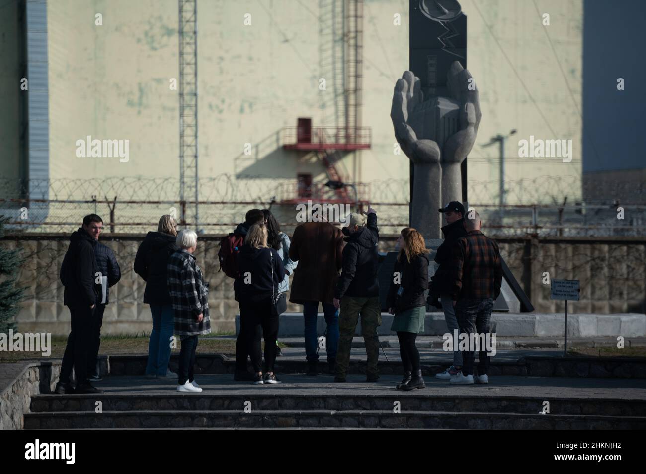 Un gruppo di turisti ascolta la loro guida fuori dal nuovo confino sicuro e il Memoriale per i Liquidatori presso la centrale nucleare di Chernobyl Foto Stock