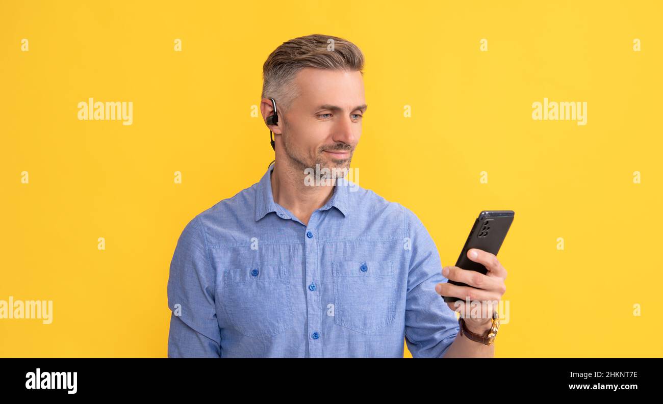 uomo sorridente che usa il telefono in cuffie su sfondo giallo, comunicazione Foto Stock