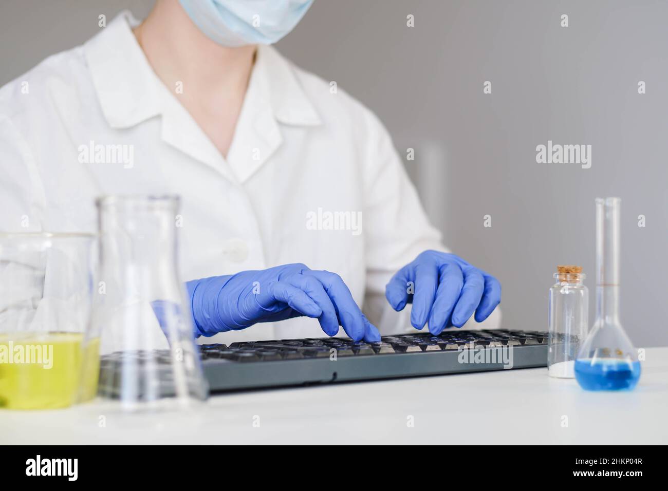 Donna scienziata in guanti che lavorano sulla tastiera al desktop in laboratorio. Foto Stock