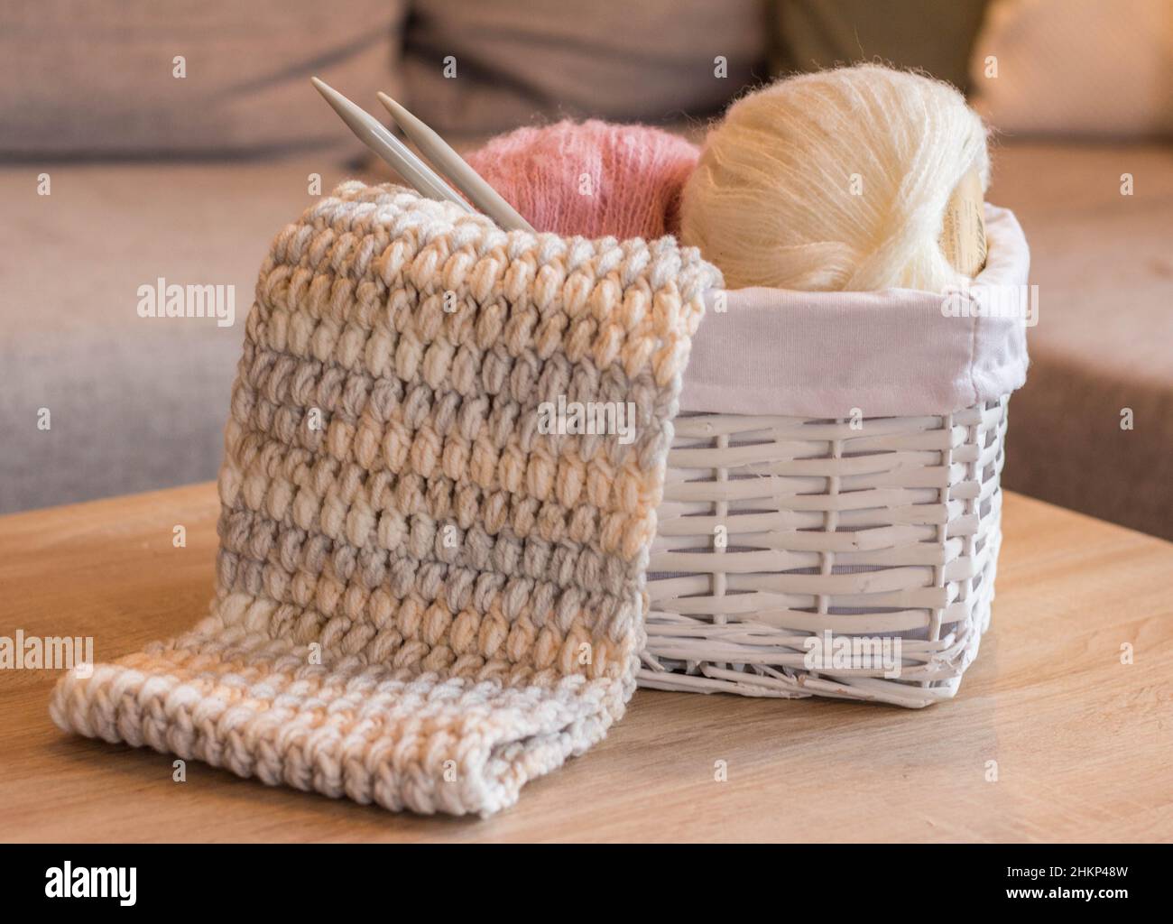 palline di lana rosa e bianca in un cestino bianco con aghi da maglieria e una sciarpa a maglia fatta a mano Foto Stock