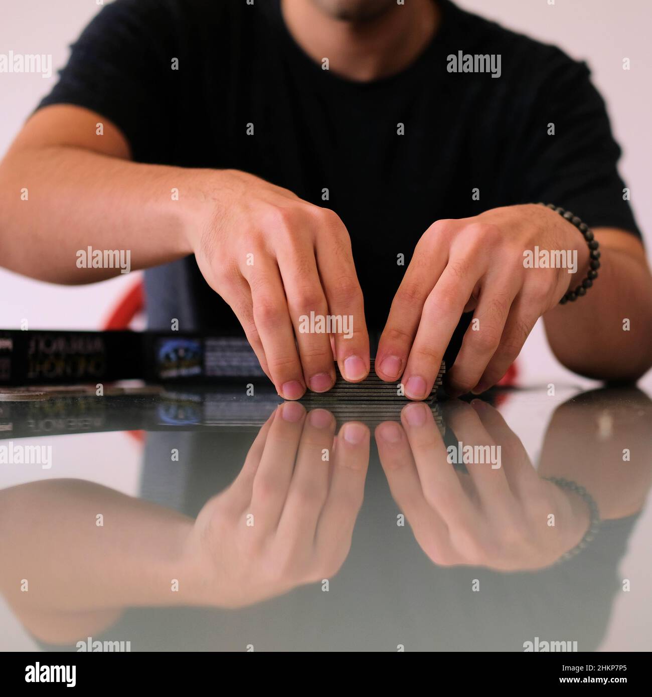 Giovane uomo mescolando e trattando carte su un tavolo da cucina riflettente in vetro a casa; gioco notte di famiglia. Foto Stock