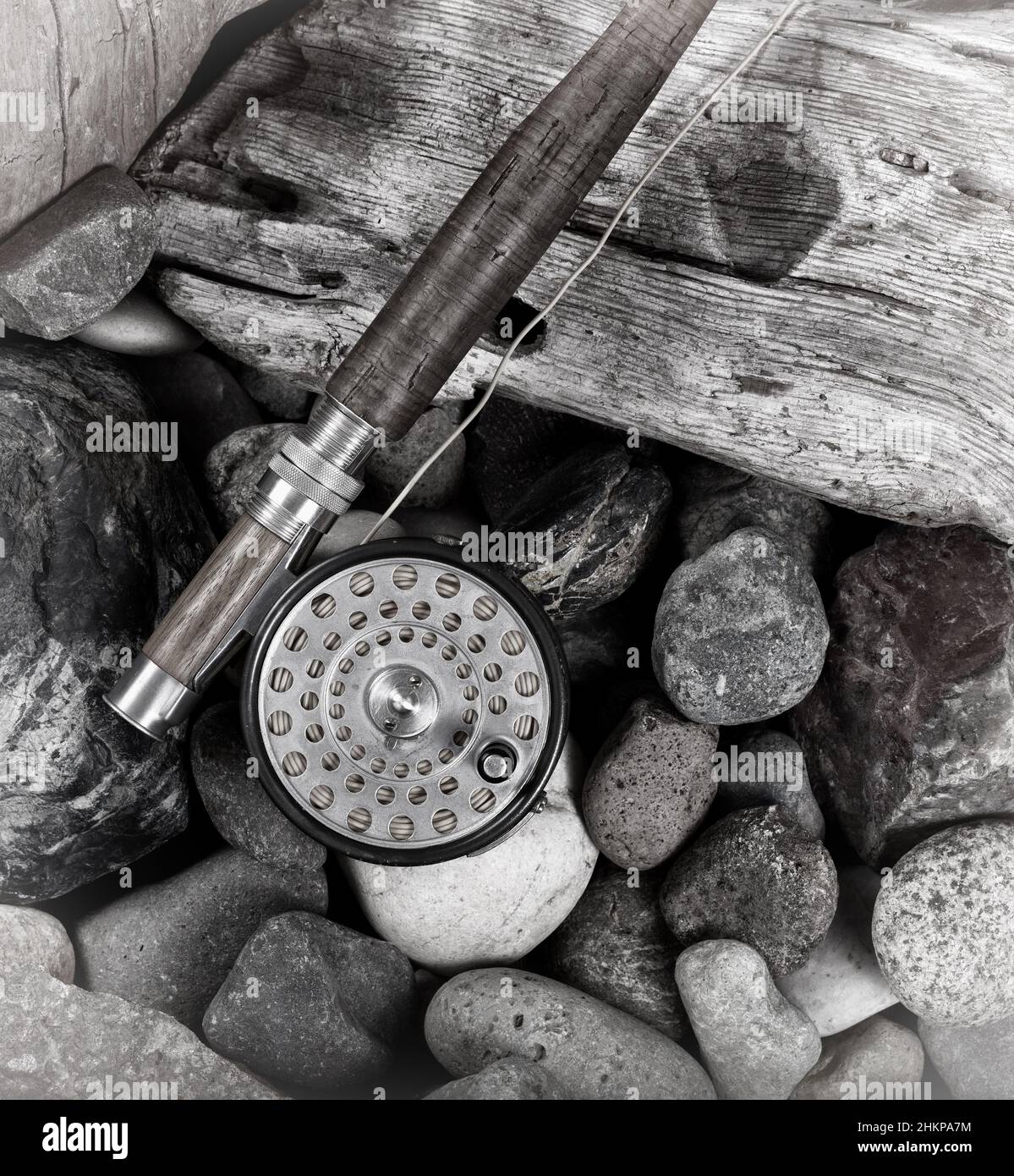 Antica asta di mosca e bobina accanto a pietra e legno di deriva con effetto vintage. Foto Stock