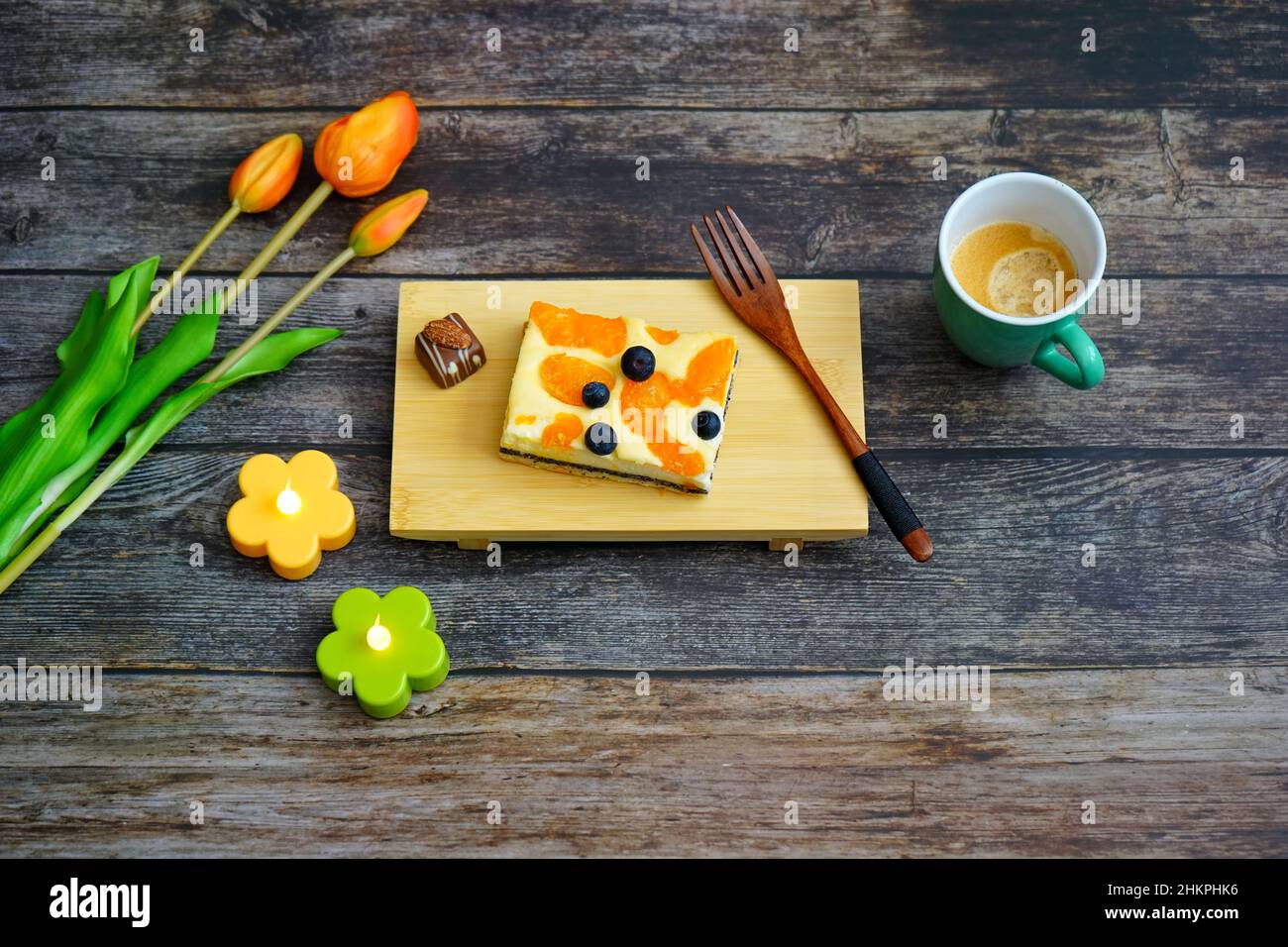 Tempo del caffè in Germania: Torta al formaggio fatta in casa e un caffè su un tavolo di legno con fiori di tulipano arancione per la decorazione. Foto Stock
